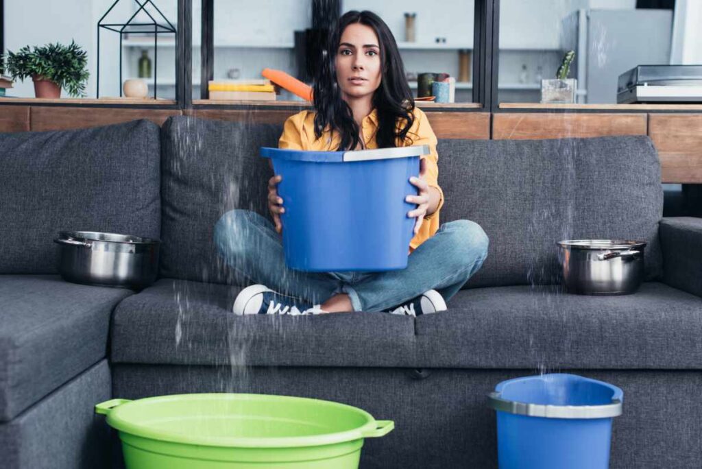 Woman holding bucket on sofa during water damage in living room